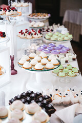 Front view of delicious cupcakes, donuts and mousse desserts on wedding candy buffet. Luxury birthday celebration catering with tasty patisserie, french recipes. Concept of yummy food on sweet bar.