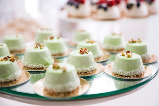 Close up of delicious decorated green glaze mousse desserts on tray. Luxury wedding catering. Patisserie french recipes. Tasty home cooking. Concept of yummy calorie food on party celebration, keto.