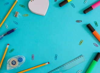 back to school concept
School supplies: markers, pencils, paper clips and more lie in a circle on a blue background with space for text in the middle, top view.