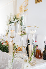 Front view of decorated table with transparent vases for wedding. Elegant birthday party with burning candles on white background. Concept of interior party decoration with fresh flowers and greenery.