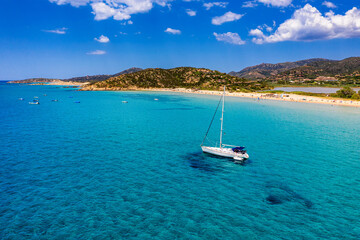 Obraz premium Yacht anchoring in crystal clear turquoise water in front of the tropical island, alternative lifestyle, living on a boat. Aerial view of yacht at anchor on turquoise water, showing luxury, wealth.