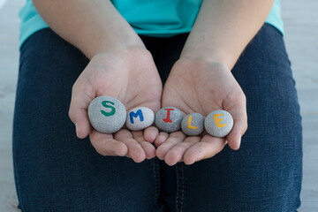 close up image of young female hands hold gray round stones with letters on them and inscription smile. Creative ideas concept. Motivating and inspiring inscriptions.