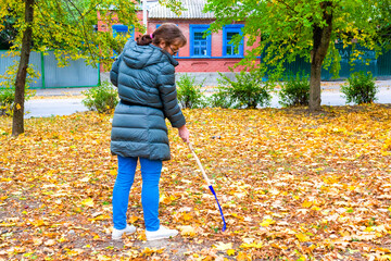 Gardener woman raking fallen leaves in backyard. Autumn seasonal work in garden.