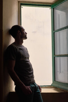 Hombre apoyado en la pared mirando por la ventana.