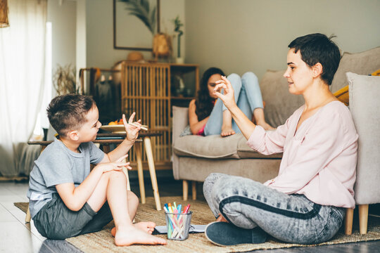 positive young mother with little son and daughter does developing exercises for fingers with wooden pencils in light living room close view