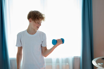 handsome happy teen boy do sport traning at home alone. use dumbbells