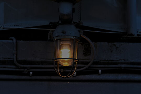 Old and weathered steel lamp glowing warm yellow light at dusk.