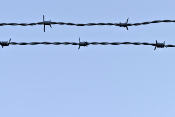 Grey barbed wire fence on a blue sky background.