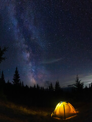 Fototapeta na wymiar Perseid meteor shower and the Milky Way in the Carpathian Mountains. Evening on a hike. tent glows on a background of night starry sky.