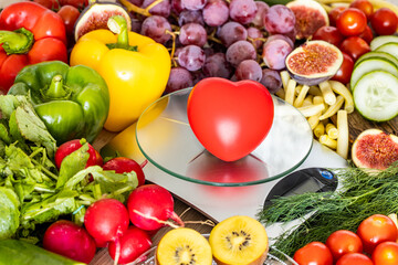 Kitchen scale with a red heart surrounded by fruits and vegetables. Concept of healthy eating and diet