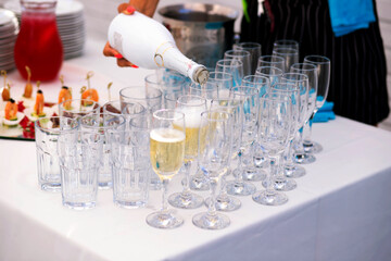 Glasses of champagne on the table for serving buffet table outdoors, waiter pouring champagne, party preparation, free space for text