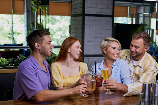 beautiful caucasian men and women hold friendly meeting in cafe, they have a great time after work, have talk. leisure, drinks, people and communication concept