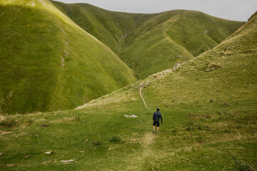 Fototapeta na wymiar green landscape of the mountain with young man walking in the pyrenees on the way to arpea cave