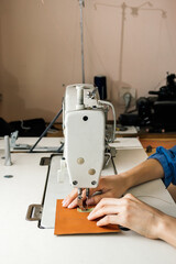 Side view of professional sewing machine in the workshop, woman's hands hold a piece of yellow leather