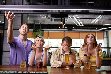 handsome young caucasian friends are sitting upset while drinking beer and cheering for sport team at the pub