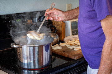Boiling pretzel dough gets lifted out of a steaming pot prior to being baked for a tasty homemade DIY snack. 

