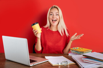 portrait of cheerful blonde lady having fun at work place isolated over red background, young...