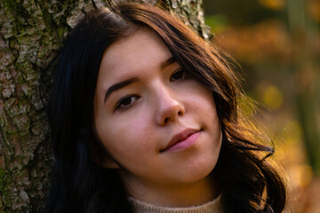 Fototapeta premium Portrait of a young pretty girl leaning her head against a tree trunk