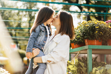 Enchanting woman kissing child in nose. Young mother expressing love to daughter on nature background.
