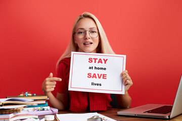confident young lady ask people to work at freelance, from home, stay home and safe the lives, she points finger at tablet. woman at office desk, look at camera isolated over red background