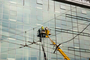 A team of assemblers of the curtain wall, being on the crane lifting platform, checks the quality of the insulation at the joints between the windows