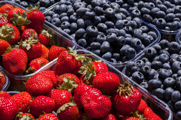 Large number of red ripe strawberry and organic blueberry on the market in small plastic containers