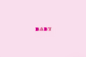 The word BABY is made of wooden letters on a pale pink background. Banner design. Baby shower concept. Photo of minimal background with beeautiful decor and place for text isolated pink background