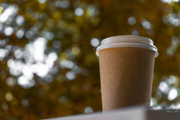 Paper disposable coffee cup on a white table with autumn bokeh.