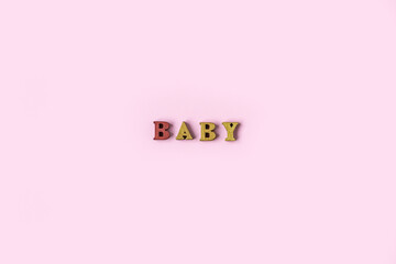 The word BABY is made of wooden letters on a pale pink background. Banner design. Baby shower...