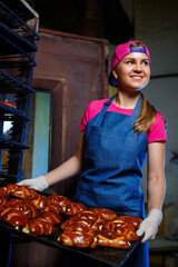 Girl baker holds a tray with hot pastries in the bakery. Production of bakery products. Fresh crispy pastry rack