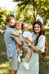 Caring parents with little kids at the park, lovely mom hold in arms joyful son, cute daughter sitting in daddy hands, family spend time together, enjoy happy moments concept