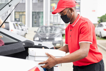confident deliveryman in red uniform puts orders in the car, he is going to carry it to clients. during quarantine