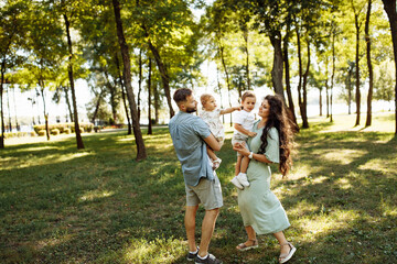 Overjoyed parents with little children walking at the park, lovely mom hold in arms joyful son, cute daughter sitting in daddy hands, family spend time together, parenthood concept