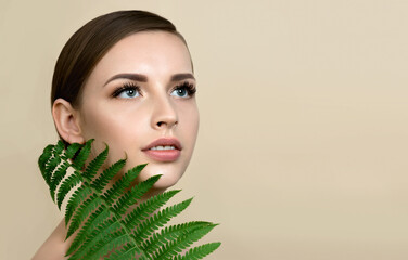 Young beautiful smiling model with natural make up and green leaf of fern.