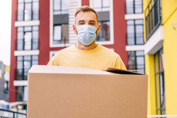 Fototapeta na wymiar Delivery man showing box in hands wearing medical mask isolated closeup. Courier's yellow shirt. Home delivery. Quarantine hero.