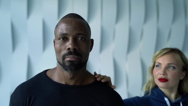 young blonde woman is seducing adult afro-american man, loving pair is embracing at room