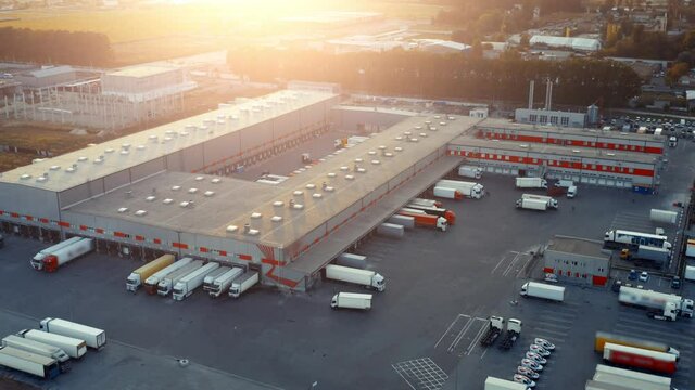 Logistics park with warehouse and loading hub. A lot of semi trucks with cargo trailers awaiting for loading/unloading goods at sunset. Aerial view 