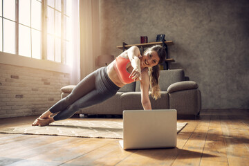 Young girl follows with a laptop a gym exercises. She is at home due to coronavirus codiv-19...