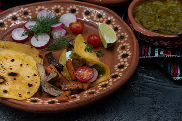 Soft corn street tacos with vegetarian filling consisting of seitan, mushrooms, carrot, chile verde and cream in traditional Mexican clay plate