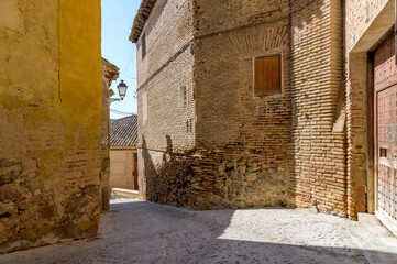 Old Street - Bright afternoon sunlight shines in a narrow street surrounded by old brick buildings in the historic city Toledo, Spain.