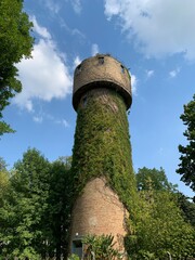 Water tower against the blue sky. The old fortress tower in the forest. Tall brick building for...