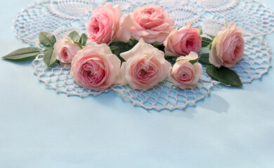 Flowers pink roses on openwork napkin on a blue paper background with space for text