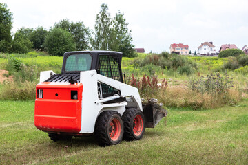 A skid steer loader clears the site for construction. Land work by the territory improvement. Machine for work in confined areas. Small tractor with a bucket for moving soil and bulk materials.