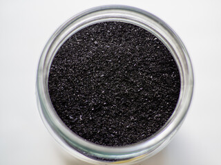 Obraz na płótnie Canvas Activated charcoal powder for cosmetic face mask in a jar top view with copy space, white back