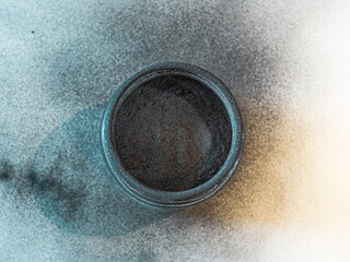 Activated carbon powder for cosmetic face mask in a jar, top view, blue shadow and white back