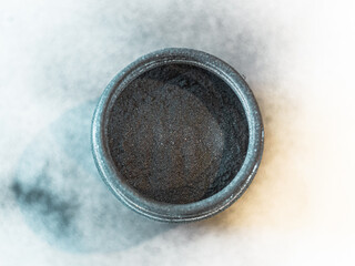 Activated carbon powder for cosmetic face mask in a jar, top view, blue shadow and white back