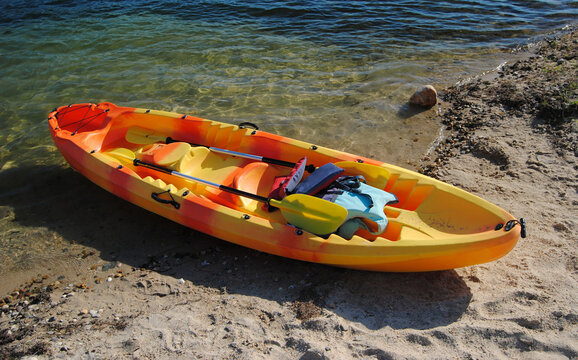 Barco a remo amarelo e vermelho parado na margem do rio com os remos e coletes salva, vidas dentro, caiaque
