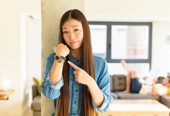 young pretty asian woman looking impatient and angry, pointing at watch, asking for punctuality,...