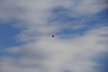 赤く真ん丸な風船が一つ浮いている、爽やかな青空と白い雲