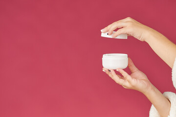 Women's hands with a jar of cream on a red and pink background